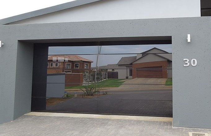 Frameless glass garage door with a sleek, modern design installed in a contemporary home, reflecting the surrounding neighborhood