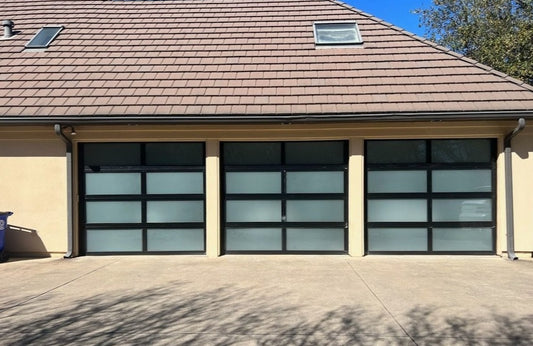 Modern triple-bay garage with frosted glass panels in sleek matte black frames, complementing a beige exterior and tiled roof, enhancing the contemporary aesthetic and curb appeal of the property